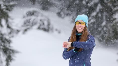 devojka u opremi za trčanje sa kapom i naočarima u snežnom parku gleda na sat