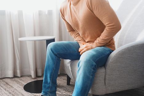 muškarac koji sedi u fotelji se drži za predeo prepona