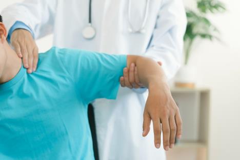 muškarac u plavoj majci sa kratkim rukavima na pregledu kod lekara koji mu drži podignutu levu ruku i pregleda mišiće vrata