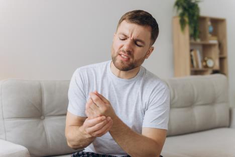 Muškarac u sivoj majci sedi na kauču i desnm rukom drži levi zglob šake