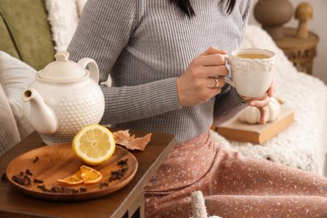žena drži u rucu šolju čaja od karanfilića, na stočiću pored čajnik, drveni tanjir, karanfilić i pola limuna