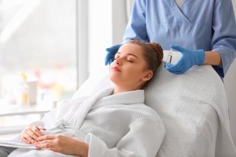 malda žena na tretmanu lepote kod dermatologa koji u rucu drži ampulu sa serumom