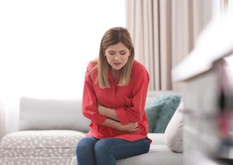 žena u crvenoj košulji sedi na kauču i drži se za bolan stomak