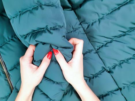 ruke žene koje proveravaju kvalitet materijala zelene perjane jakne