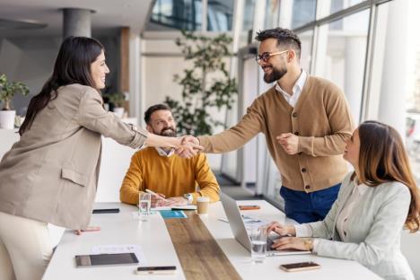 četiri osobe u sali za sastanke od kojih se dve rukuju uz osmeh