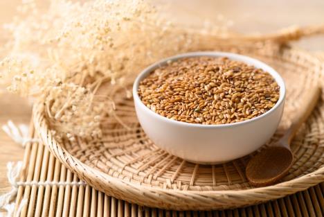 činija sa zlatnim lanenim semenom na poslužavniku od trske, drvena kašičica i suva biljka pored