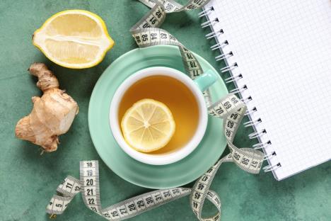 želena šoljia čaja od đumbira i limuna, na stolu krojački metar i sveska, koncept mršavljenje