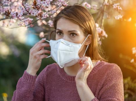mlada žena alegičana na polen drveća stavlja masku na lice