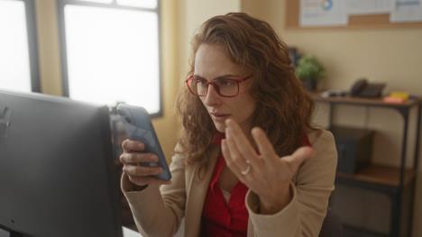 Žena zbunjeno gleda u telefon u svojoj kancelariji