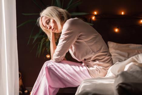 iscrpljena žena sedi na krevetu i ne može da spava