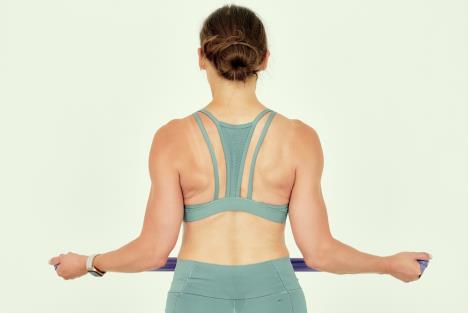 devojka u sportskoj opremi, okrenuta leđima vežba gornji deo leđa i lopatice