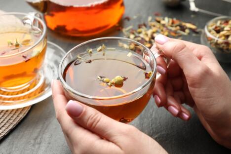 krupan plan ženskih ruku koje drže staklenu šolju sa biljnim čajem