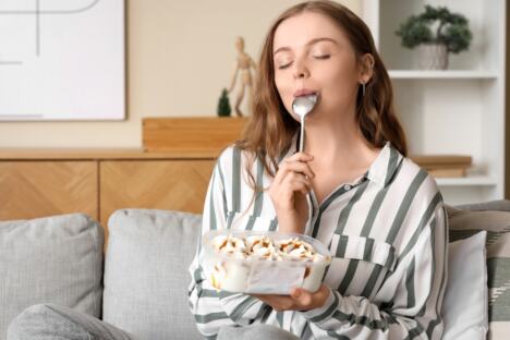 devojka sedi u dnevnoj sobi na kauču i jede sladoled iz kutije kašikom