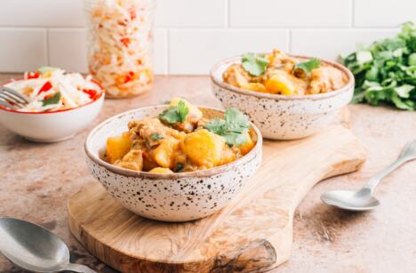 dve činije na stolu sa krompir paprikašem, kašike, mešana salata, veza peršuna