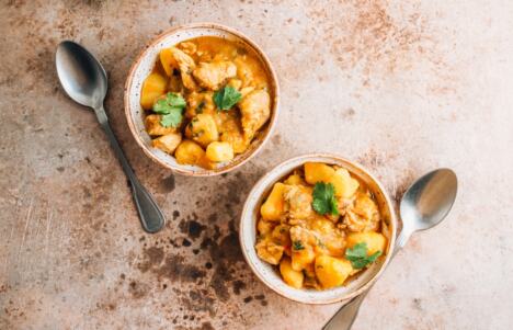 dve činije krompir paprikaša sa kašikama na stolu