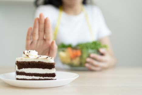 žena odbija parče torte jednom rukom, drugom pridržava činiju sa salatom