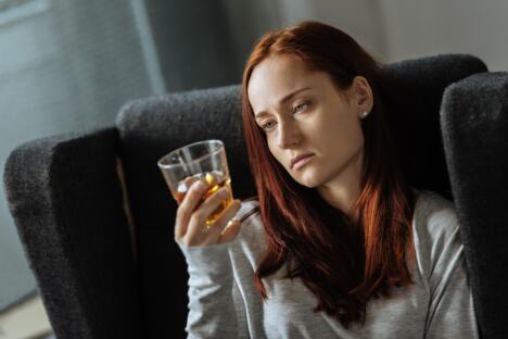 Tužna žena sedi na krevetu i pije alkohol