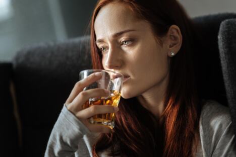Tužna žena sedi na krevetu i pije alkohol