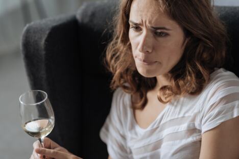 Tužna žena sedi na krevetu i pije alkohol