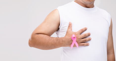 muškarac se drži za grudi, roze traka, rak dojke kod muškaraca