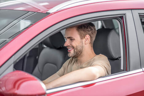 Car driving. Smiling young male driving red car, putting elbow out of window