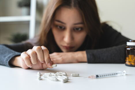 devojka za stolom na kome se nalazi droga, tablete i špric