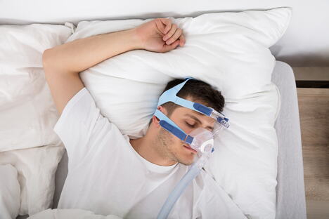 muškarac u krevetu sa CPAP aparatom, koncept apneja u snu