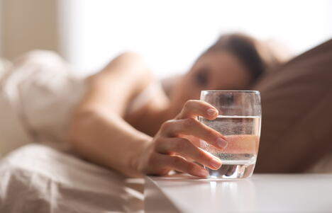 žena u krevetu poseže za čašom vode na noćnom stočiću