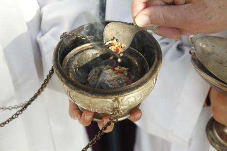 U ruci drži kadionicu i preko briketa posipa tamjan