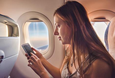 stockphototouristwomansittingnearairplanewindowatsunsetandusingmobilephoneduringflight528970954.jpg