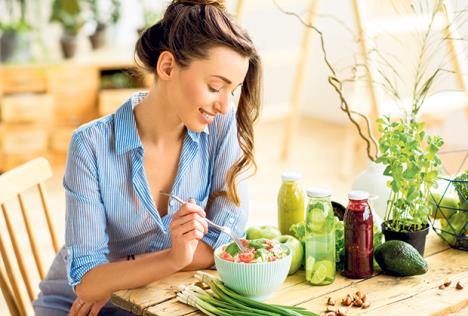 stockphotoyoungandhappywomaneatinghealthysaladsittingonthetablewithgreenfreshingredientsindoors622381799.jpg