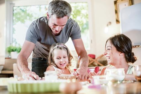 stockphotoafouryearsoldblondegirliscookingsmallcakeswithhermotherandgreyhairedfatherina367324376.jpg