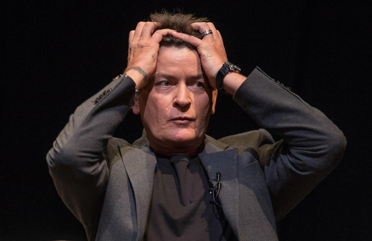 Čarli Šin u odelu, drži se sa obe ruke za glavu.jpg